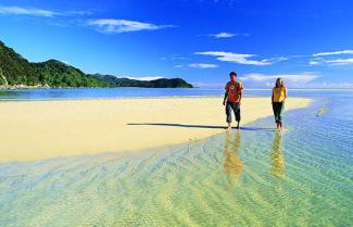 A couple wading through the warm waters as they hike the Tasman Track.